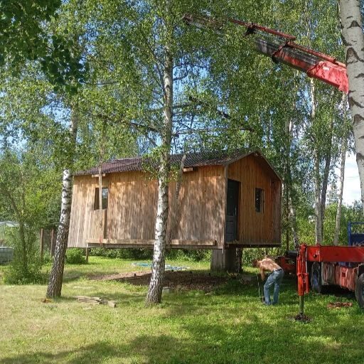 Manipulators paceļ koka vasarnīcas moduli starp kokiem. Ar jaudīgo manipulatoru veicam sarežģītus darbus grūti pieejamās vietās