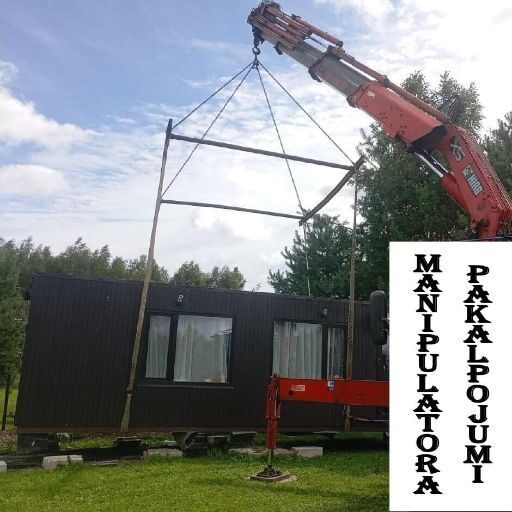 Manipulators paceļ un pārvieto moduļu māju, demonstrējot manipulatora pakalpojumus un liela izmēra kravu transportēšanu